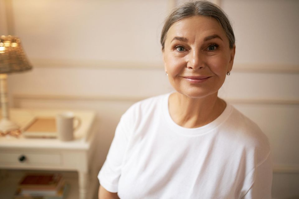 Postmenopause: Eine hübsche, etwa 60-jährige, lächelnde Frau im weißen T-Shirt