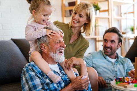 Kind auf Schultern von Großvater und lachenden Eltern daneben