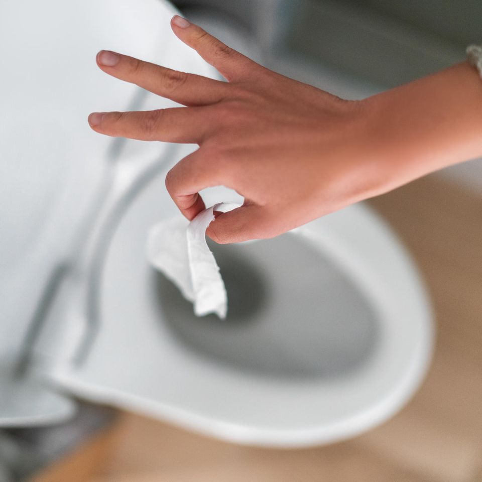Eine Hand wirft ein Stück Toilettenpapier in eine Kloschüssel
