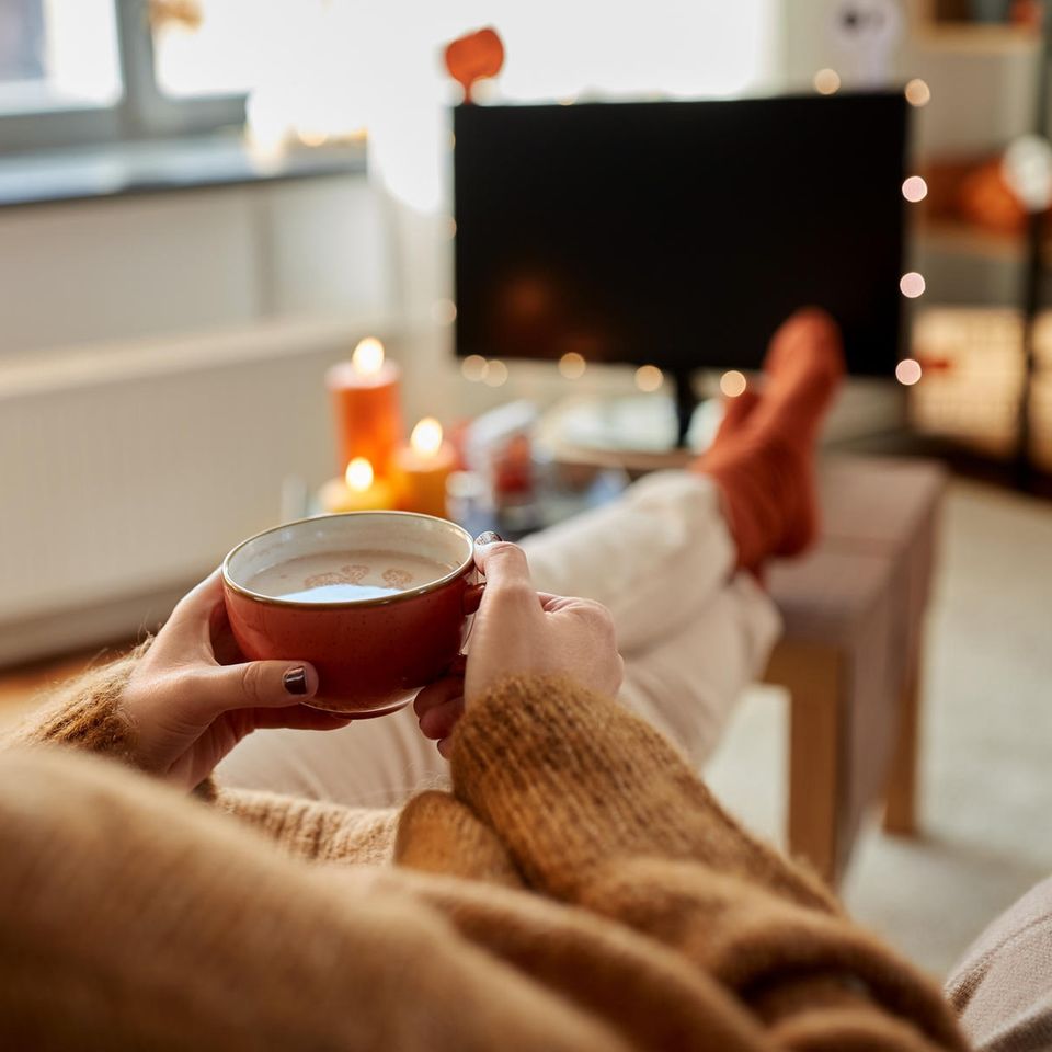 Notting Hill & Co.: Herbstoutfits unserer liebsten Rom-Coms, Frau vor dem TV mit Teetasse