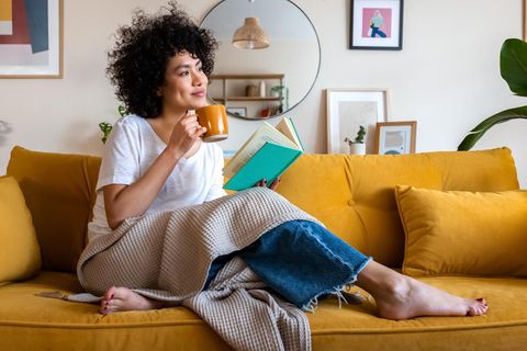 Eine Frau sitzt mit Buch und Tasse auf dem Sofa