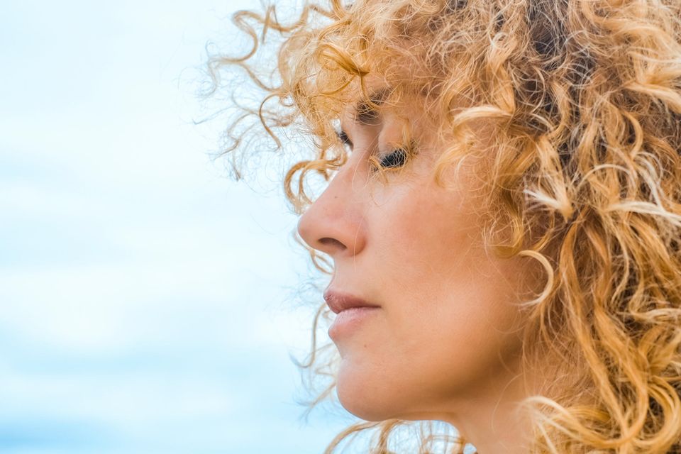 Frau mit blonden locken im Profil hat geschlossene Augen vor blauen Himmel