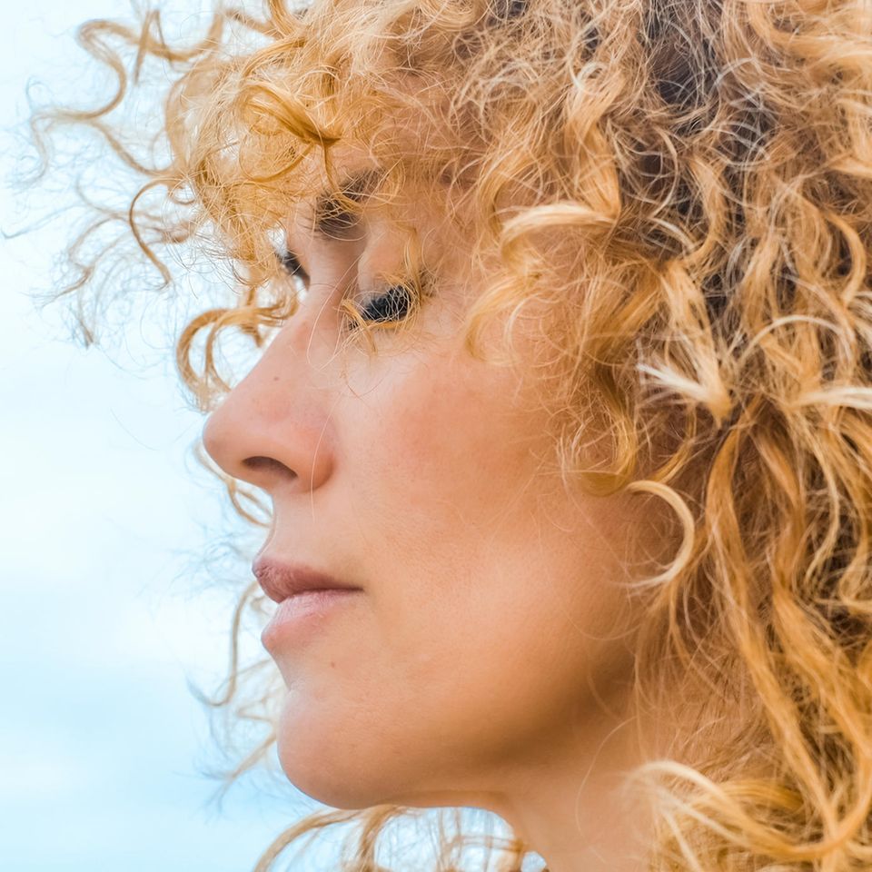 Frau mit blonden locken im Profil hat geschlossene Augen vor blauen Himmel