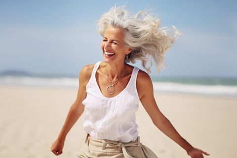 Fröhlichere ältere Dame läuft am Strand entlang