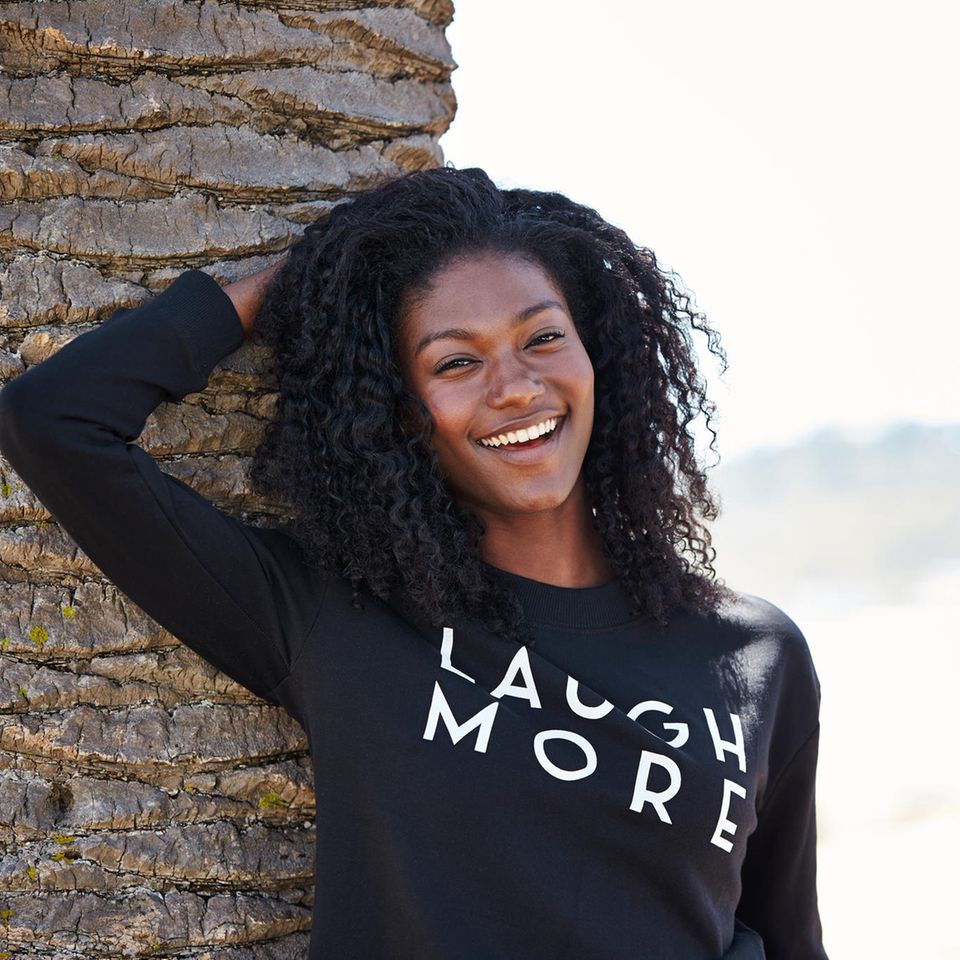 Das perfekte Statement-Sweatshirt: Ganz einfach kombiniert, lachende Frau neben einer Palme