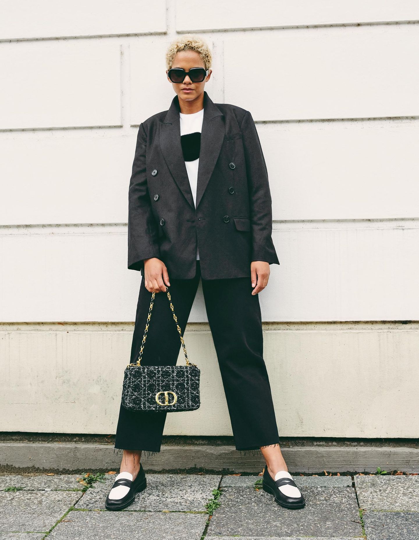 Für einen klassischen Business Casual Look ist der doppelreihige Blazer von &Other Stories mit der fransigen Jeans von Lovjoi perfekt geeignet. Um einen farblichen Kontrast zu setzen kombiniert das Model einen weißes T-Shirt mit schwarzem Plüsch-Punkt und stylische Loafer. Die Prada-Sonnenbrille sowie die Handtasche von Christian Dior machen den eleganten Look komplett. 