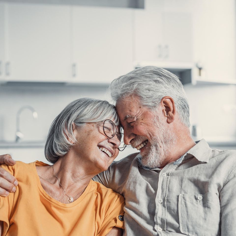 Glückliches, älteres Ehepaar sitzt lachend auf einer Couch