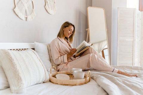 Digital Detox: Frau sitzt ohne Handy im Bett und liest ein Buch