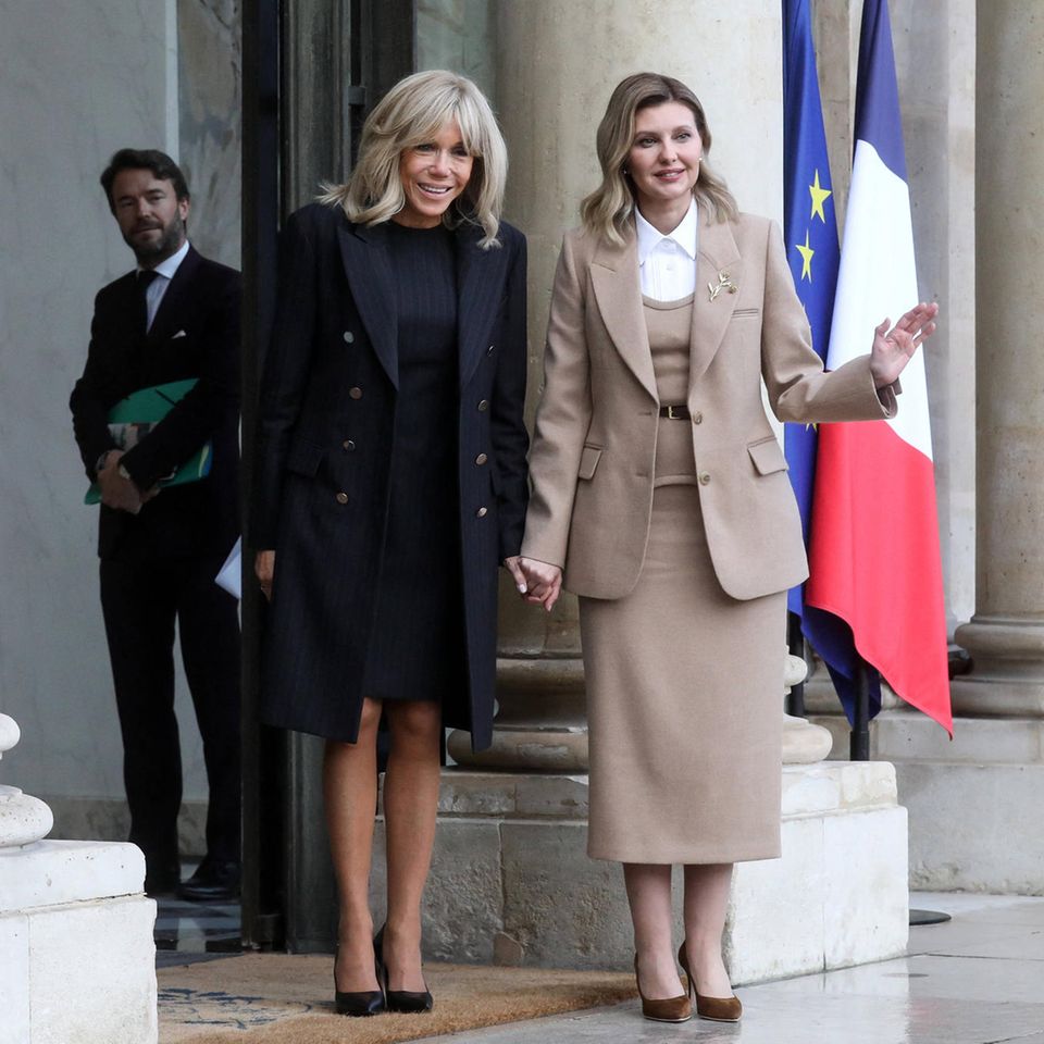 Die Première Dame von Paris empfängt Olena Zelenska im Élysée-Palast. Während die Frau des ukrainischen Präsidentens in einem beigefarbenen Ensemble anreist, empfängt die Gastgeberin den Besuch in einem dunkelblau-grün gestreiften Kleid mit passendem Mantel. Die zwei scheinen gute Freunde zu sein und halten sich für die Fotografen an den Händen. 