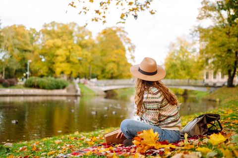 Die schönsten Herbstzitate: Frau sitzt im Herbst am See