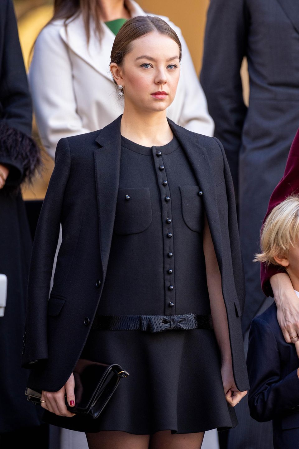 Bei der Militärparade am Nationalfeiertag in Monte-Carlo setzt Prinzessin Alexandra auf Céline. Das bestickte Chelsea-Minikleid aus Diagonal Wolle bezaubert mit Taschen-Details und einer Schleife. Darüber kombiniert sie einen einfachen schwarzen Blazer. 