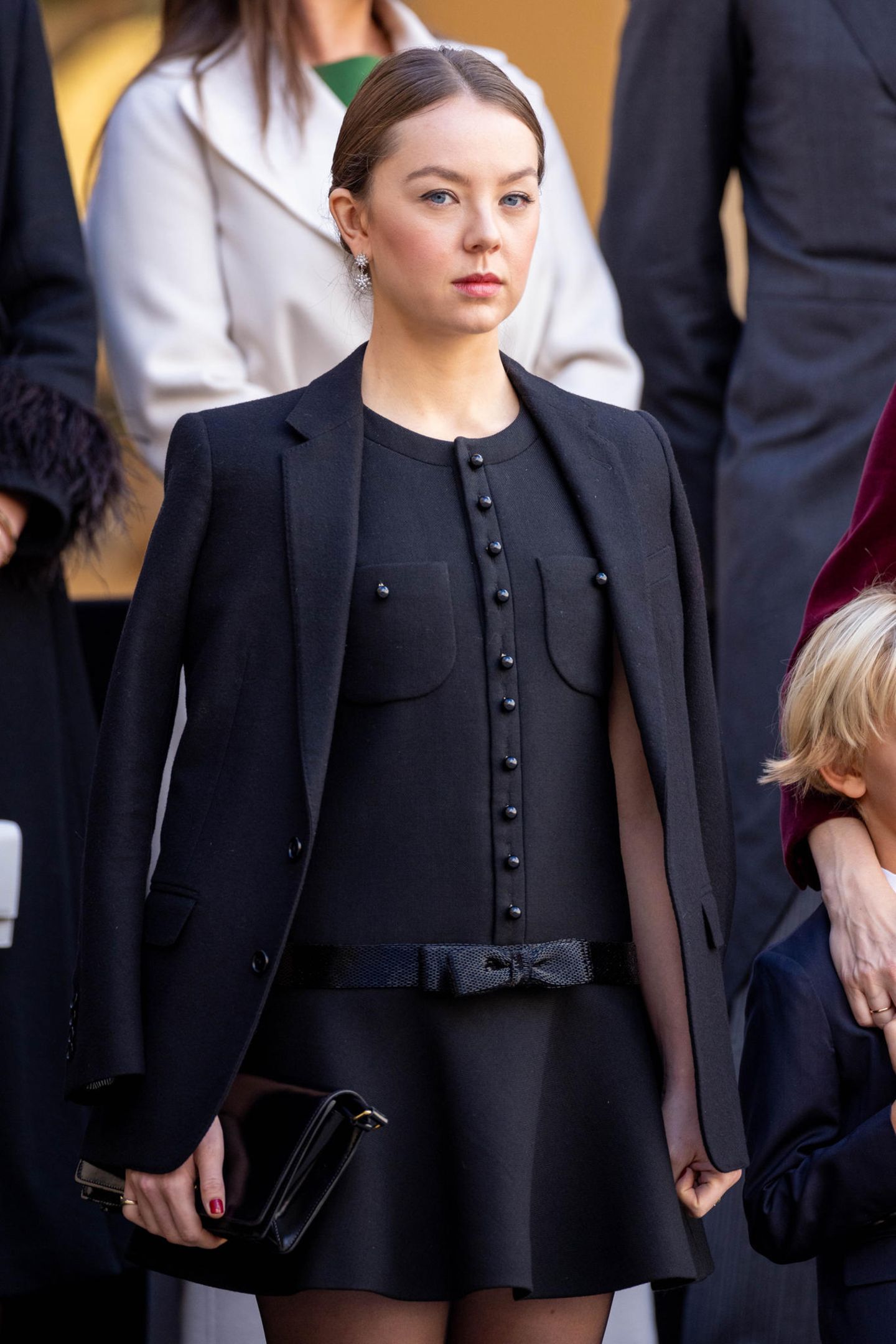 Bei der Militärparade am Nationalfeiertag in Monte-Carlo setzt Prinzessin Alexandra auf Céline. Das bestickte Chelsea-Minikleid aus Diagonal Wolle bezaubert mit Taschen-Details und einer Schleife. Darüber kombiniert sie einen einfachen schwarzen Blazer. 