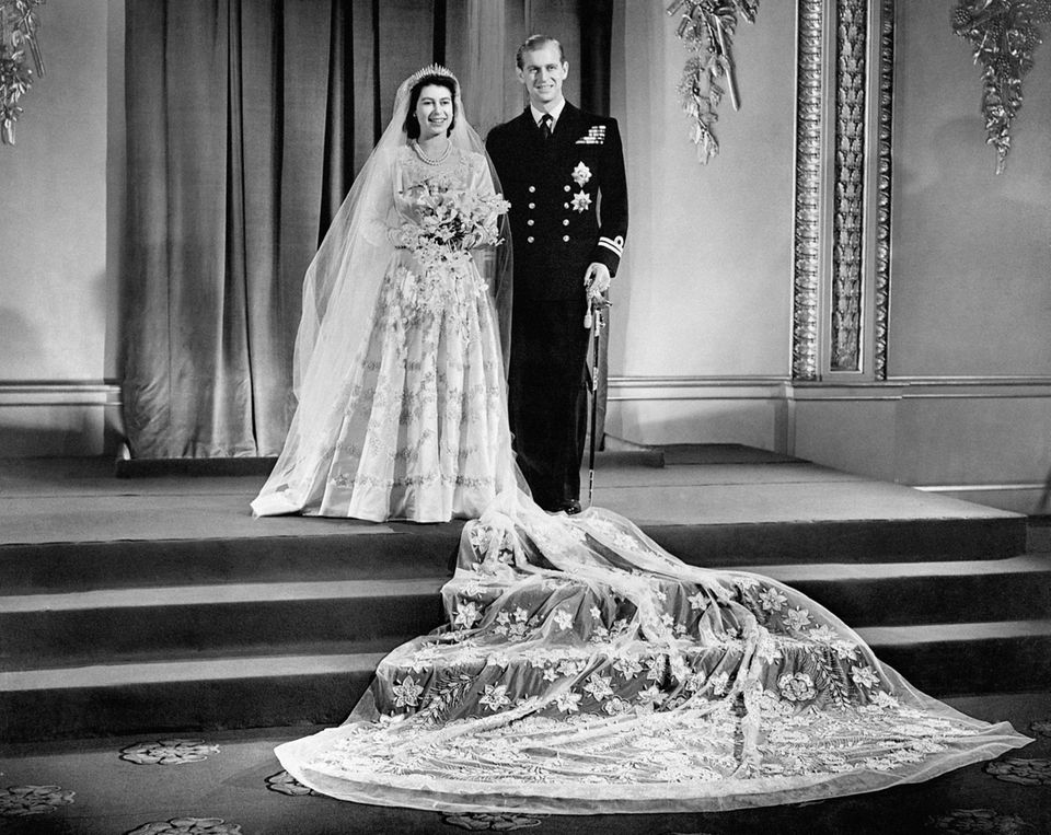 Am 20. November 1947 treten Queen Elizabeth und Prinz Philip vor den Traualtar. Norman Hartnell entwarf für die im September 2022 verstorbene Queen ein Kleid aus weißem Satin mit einem hohen Kragen und einer langen, mit Blumen bestickter Schleppe, die für die offiziellen Fotos dramatisch auf den Stufen vorm Brautpaar drapiert wurde. 