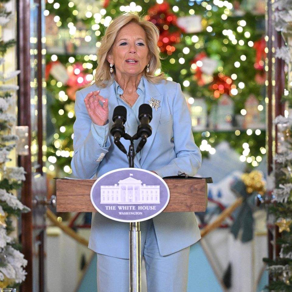Dr. Jill Biden begrüßt in einem zarten Himmelblau die Presse zur Enthüllung der Weihnachtsdekoration des Weißen Hauses. Hose, Bluse und Blazer sind gekonnt aufeinander abgestimmt – der perfekte Dreiklang. Dazu kombiniert die eine Diamant-Brosche, die an eine Schneeflocke erinnert sowie passende Ohrringe. Ungewohnt ist der hellblaue Lidschatten auf den Augen, hält sie sich doch sonst beim Make-up eher zurück. 