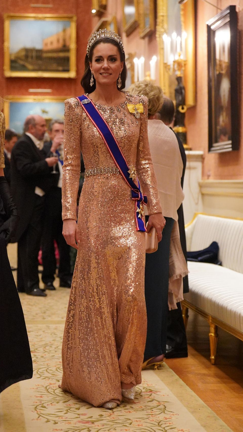 Beim Empfang für das Diplomatische Corps im Buckingham Palace strahlt Catherine, Prinzessin von Wales, mit ihrer Tiara um die Wette. Wie so oft entscheidet sich Kate für den festlichen Anlass für ein lachsfarbenes Paillettenkleid ihrer Lieblingsdesignerin Jenny Packham, das gleiche Kleid, das sie bei der Hochzeit von Kronprinz Hussein von Jordanien im Juni dieses Jahres trug. Doch für Kate ist ein Eye-Catcher nicht genug. Sie begeistert nicht nur mit eleganten Diamantohrringen, sondern auch ihre Schuhe funkeln majestätisch vor sich hin.