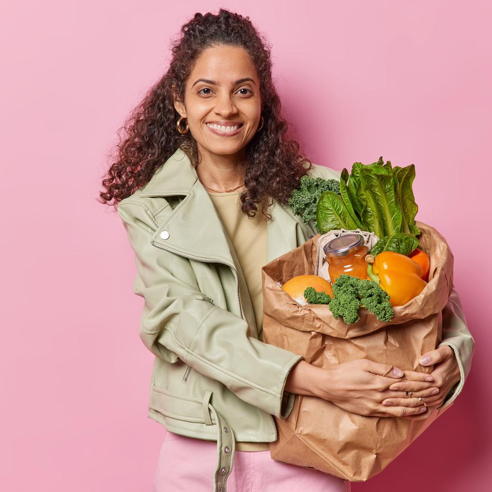 Ernährung in den Wechseljahren: Frau mit dunklen Locken hält eine große Papiertüte mit Gemüse im Arm