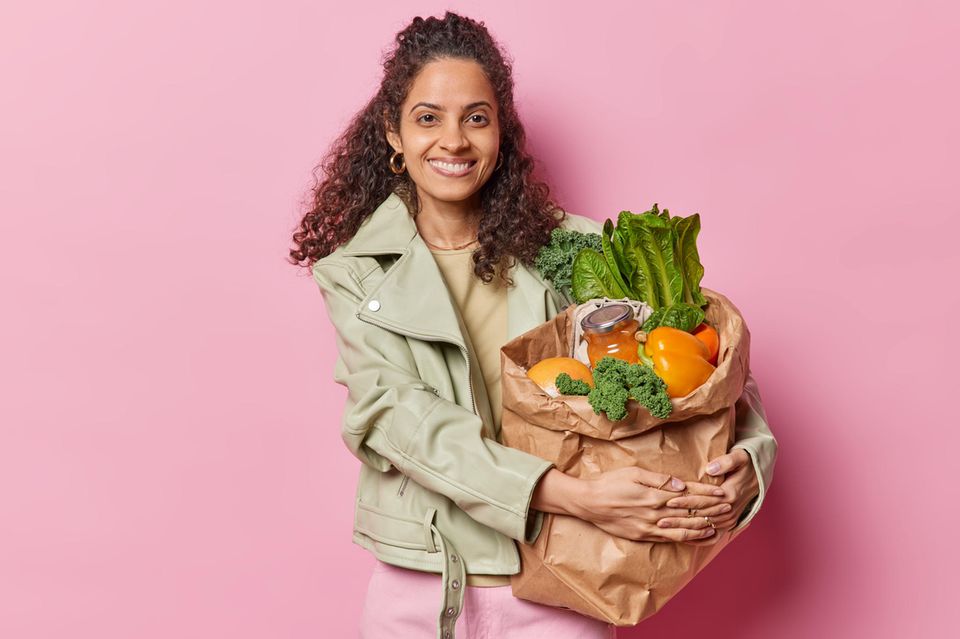 Ernährung in den Wechseljahren: Frau mit dunklen Locken hält eine große Papiertüte mit Gemüse im Arm