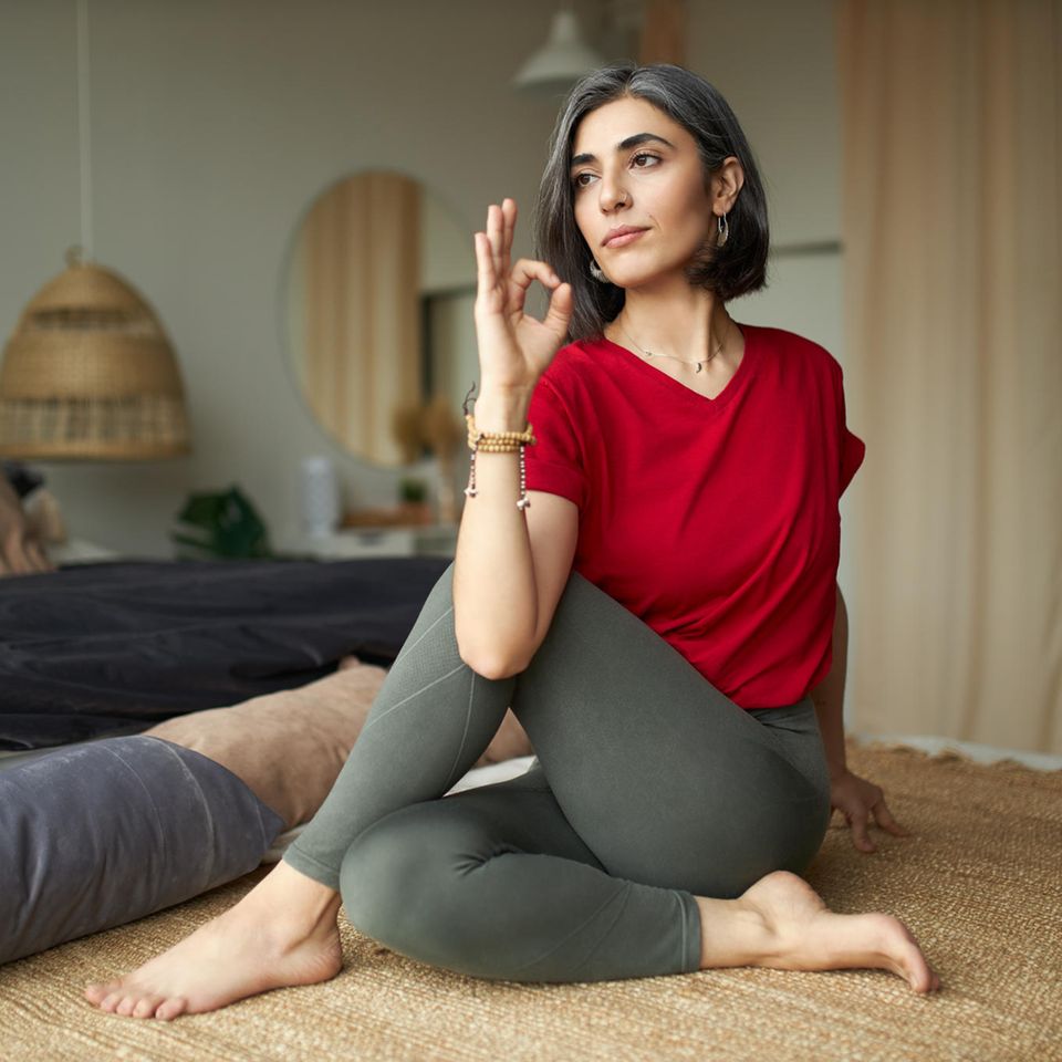 Hormon-Yoga: Eine Frau mit leicht ergrauten Haarsträhnen in der Yoga-Haltung Drehsitz