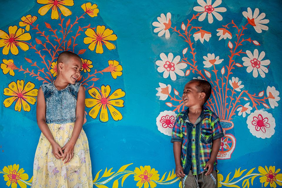 Zwei Kinder vor einer bemalten Wand lachen sich glücklick an