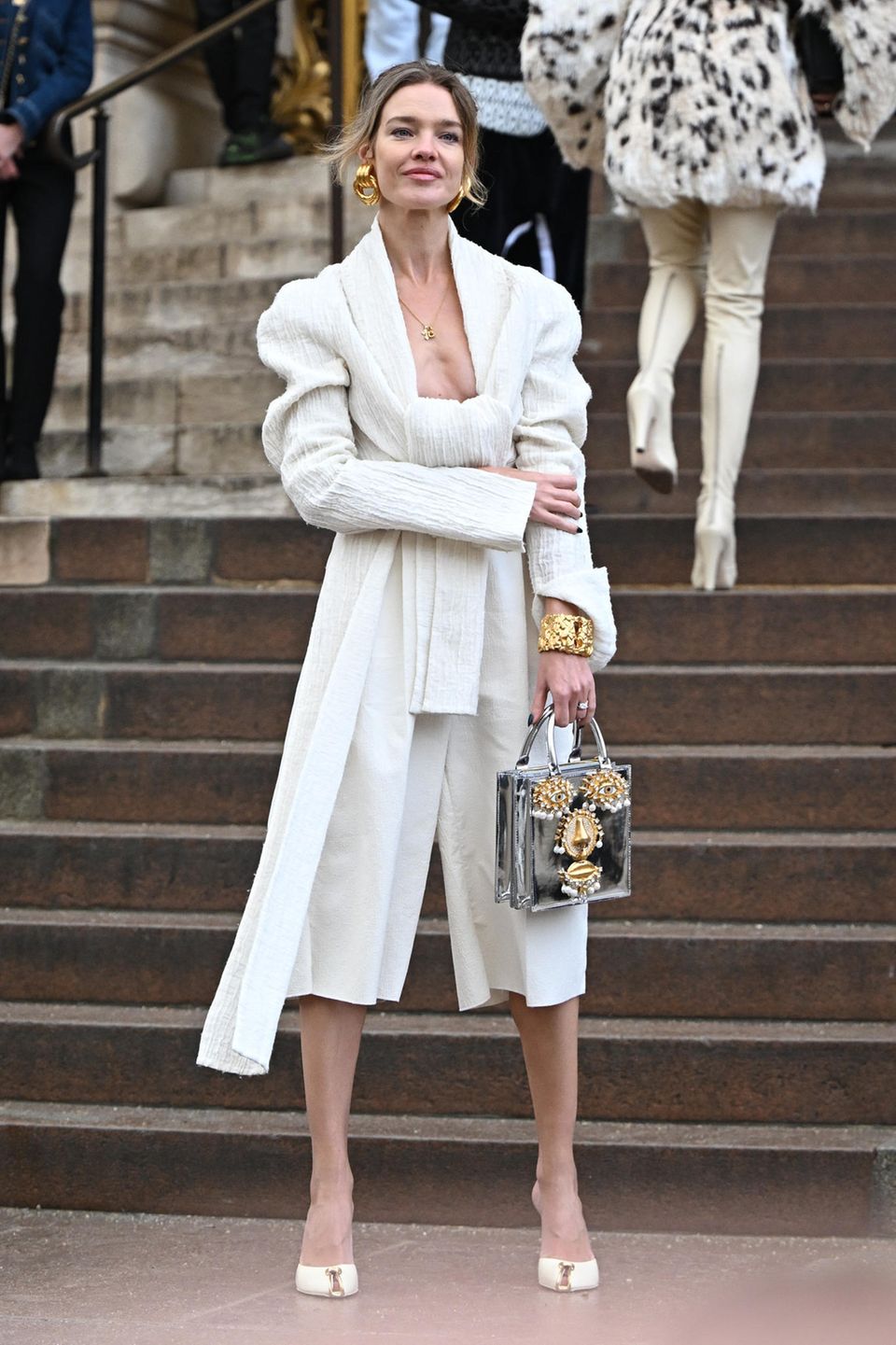 Ärmel hochgekrempelt – jetzt wird hohe Fashionkunst gezeigt. Natalia Vodianova setzt zur tief ausgeschnittenen Creme-Bluse auf Midi-Culotte, auffälligen Schmuck und silberne Gesichtstasche. Elegant!
