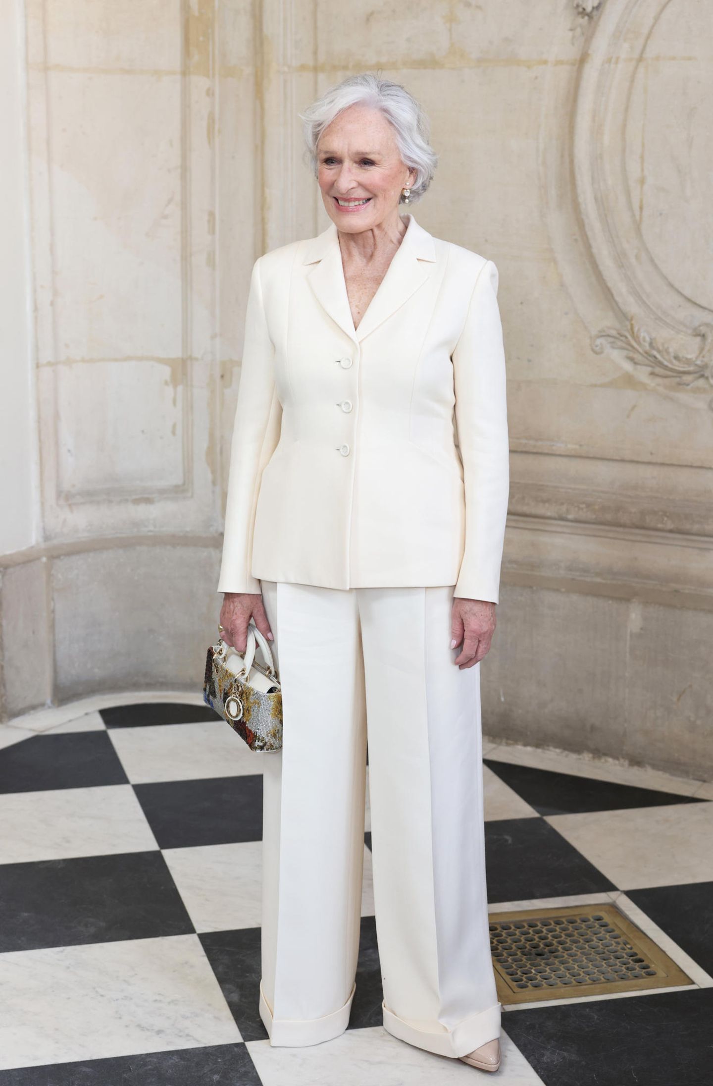 Ein weiteres bekanntes Gesicht bei der Fashion-Show von Dior: Oscar-Preisträgerin Glenn Close kommt im weißen, texturierten Hosenanzug mit umgeschlagenem Saum und bunter Dior-Tasche und gleicht damit einer griechischen Business-Göttin. 