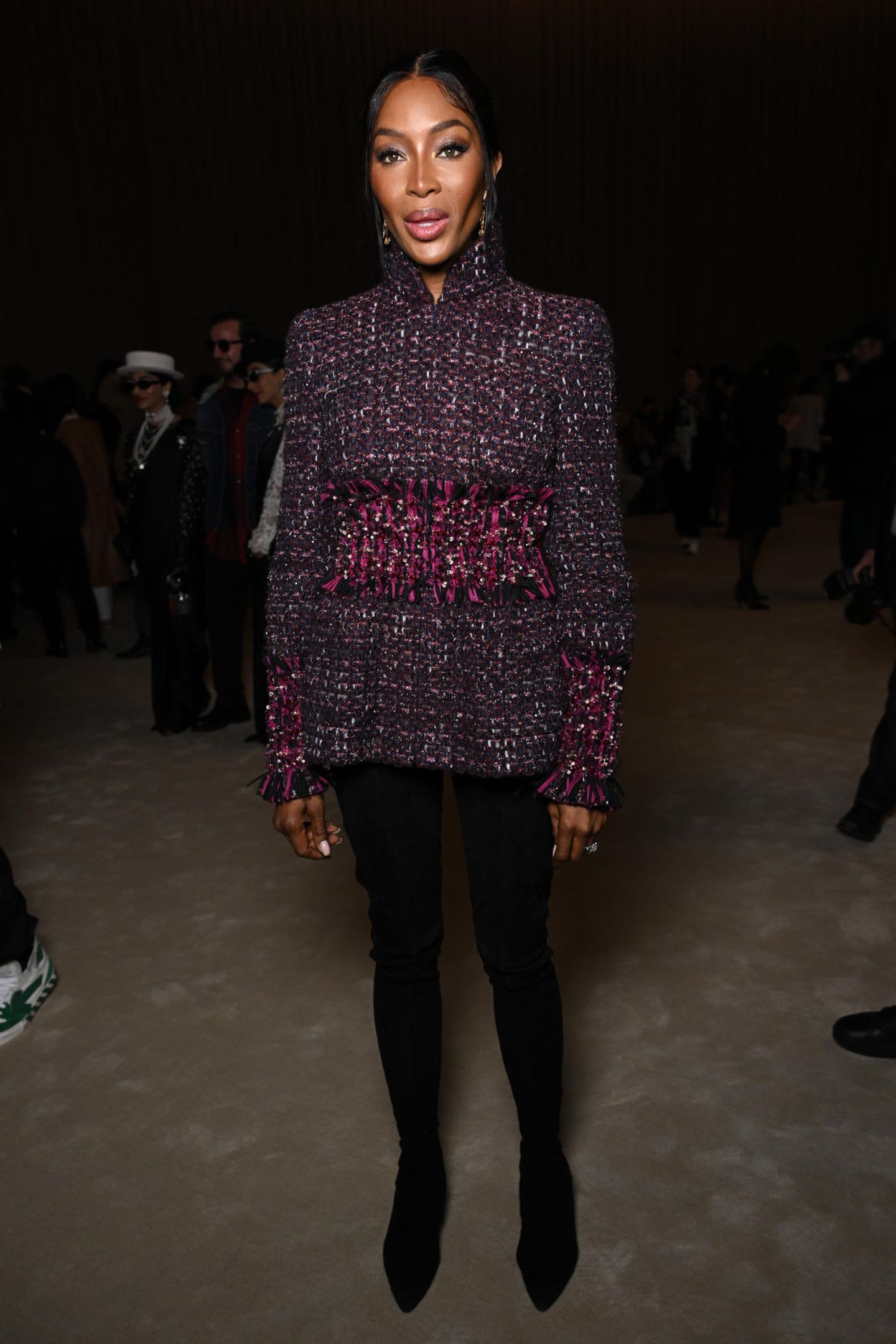 Wie aus einem Guss! Naomi Campbell wählt für die Chanel Haute Couture Show gedeckte Farben und kombiniert eine eng anliegende Hose mit integrierten Stiefeln mit hochgeschlossener weinroter Jacke und langen Ohrringen. 