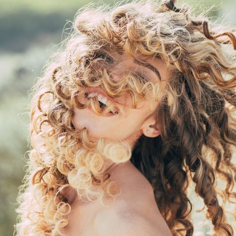 Curly Hair Methode: Eine junge Frau mit Naturlocken lacht in die Kamera