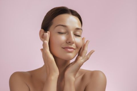 Make-up für trockene Haut: Frau mit ebenmäßigem Teint fasst sich zart an die Wangen