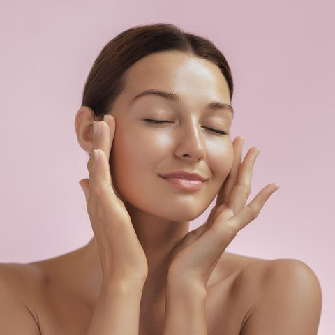 Make-up für trockene Haut: Frau mit ebenmäßigem Teint fasst sich zart an die Wangen