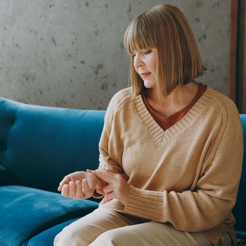 Herzrasen in den Wechseljahren: Eine mittelalte Frau sitzt auf dem Sofa und fühlt ihren Puls.