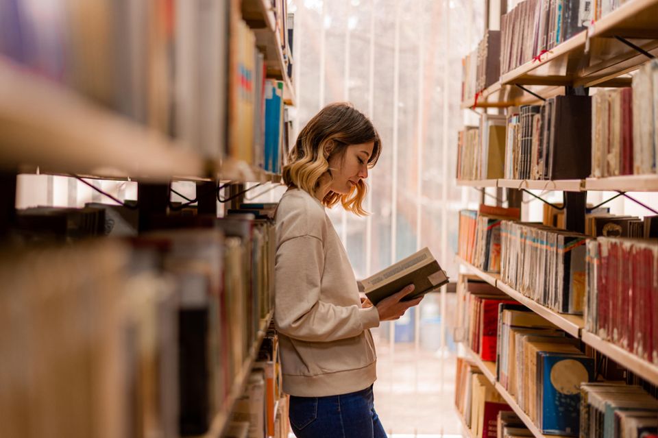 Frau liest zwischen Bücherregalen