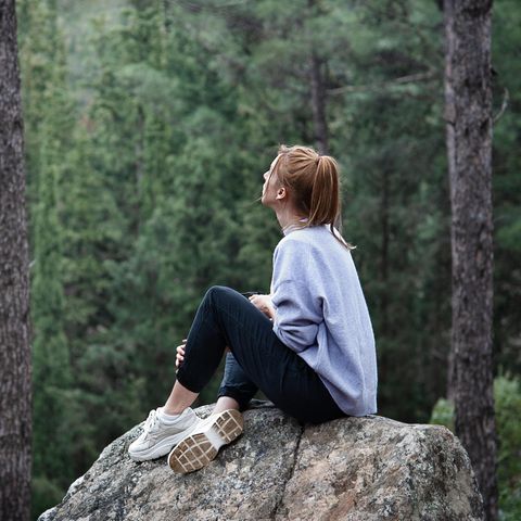 Eine Frau sitzt auf einem Stein im Wald