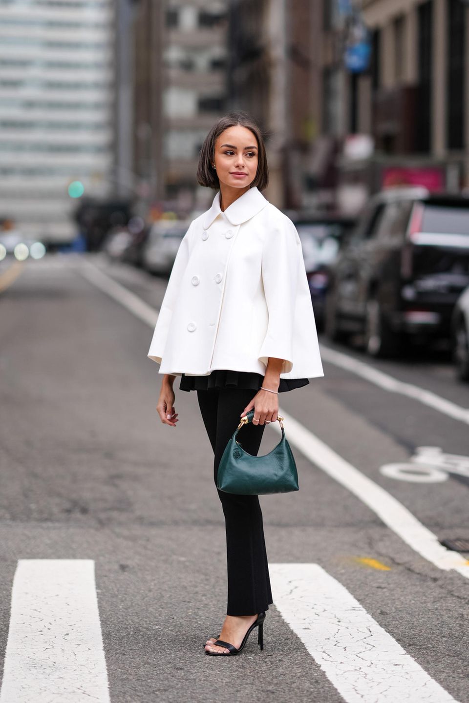 Dieser Gast präsentiert sich vor den Modenschauen in New York in einer eleganten, ausgestellten, weißen Jacke. Dazu trägt sie eine schmale Straight-Leg-Hose, Riemchensandaletten und eine grüne Tasche. 