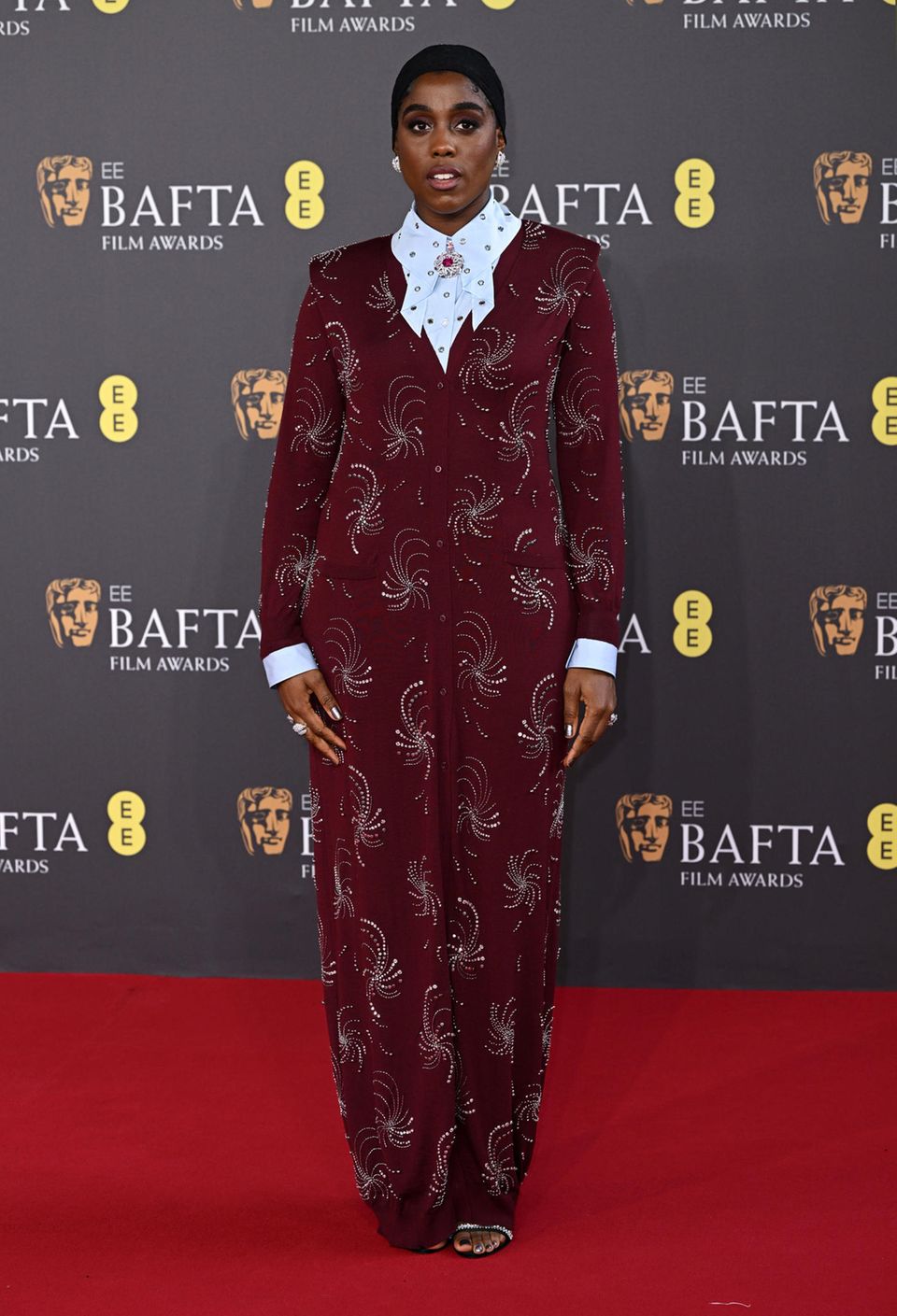 Lashana Lynch begeistert im bordeauxroten, strasssteinbesetzten Prada-Look bei den BAFTAs. 