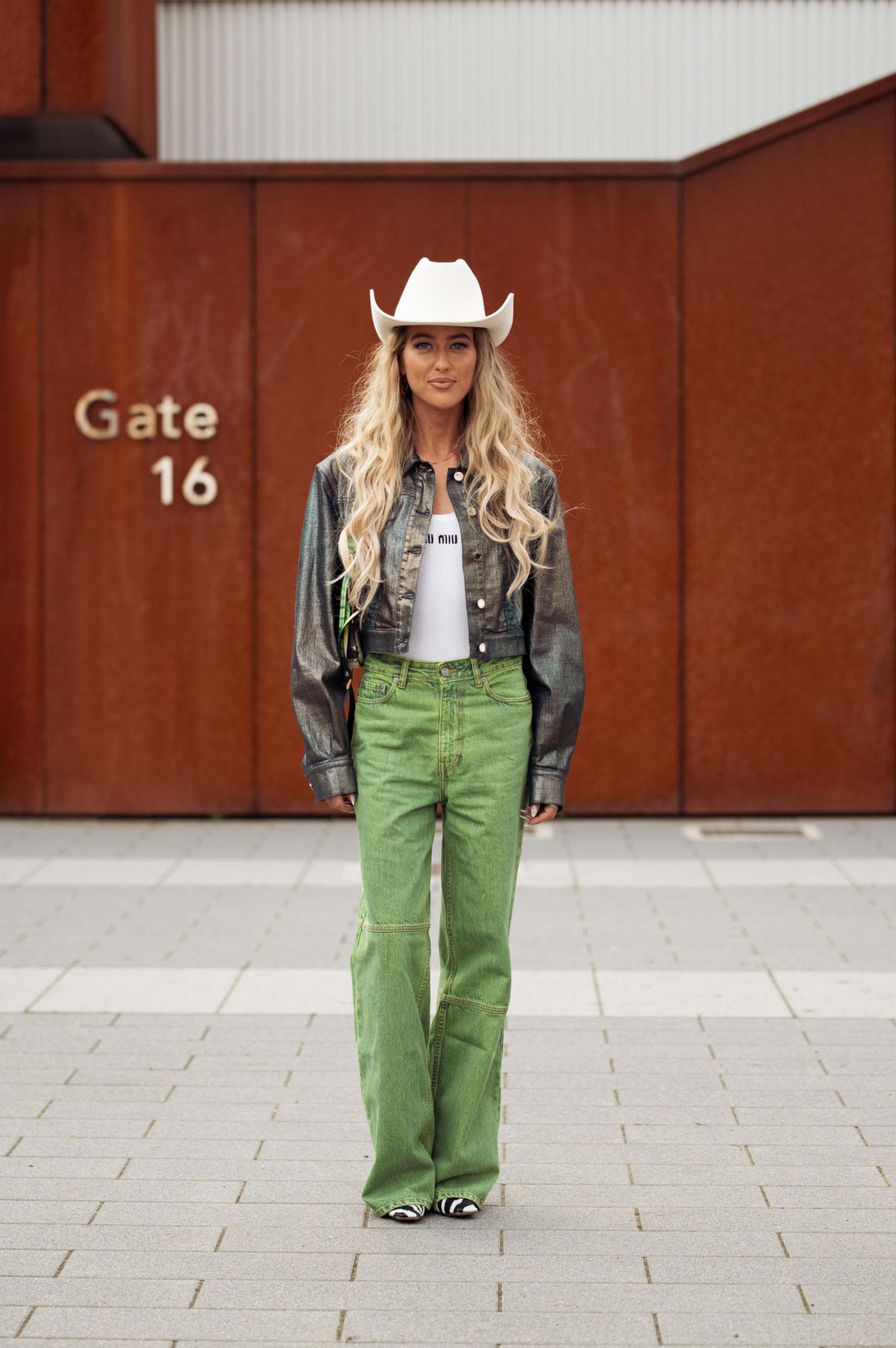 Ganz im Western-Look besucht Emili Sindlev die Alberta Ferretti Show in Mailand. Sie trägt einen weißen Cowboyhut, eine gecroppte Lederjacke in Holo-Optik, ein Miu-Miu-Top und eine grüne Jeans. Zebra-Schuhe machen das Outfit komplett. 