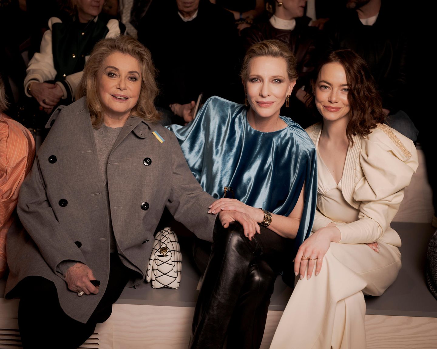 Auch Catherine Deneuve nimmt neben Cate Blanchett und Emma Stone ihren Platz ein. So ganz angekommen ist sie im grauen Mantel mit zweireihiger Knopfleiste noch nicht. Der offene Mantel offenbart jedoch auch etwas von ihrem lässigen Look: Strickpullover und schwarze Hose, mehr braucht es nicht. 