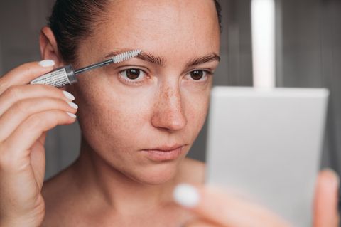 Augenbrauen-Serum: Eine Frau trägt mit einer kleinen Bürste ein Serum auf ihre Augenbraue 1.5004