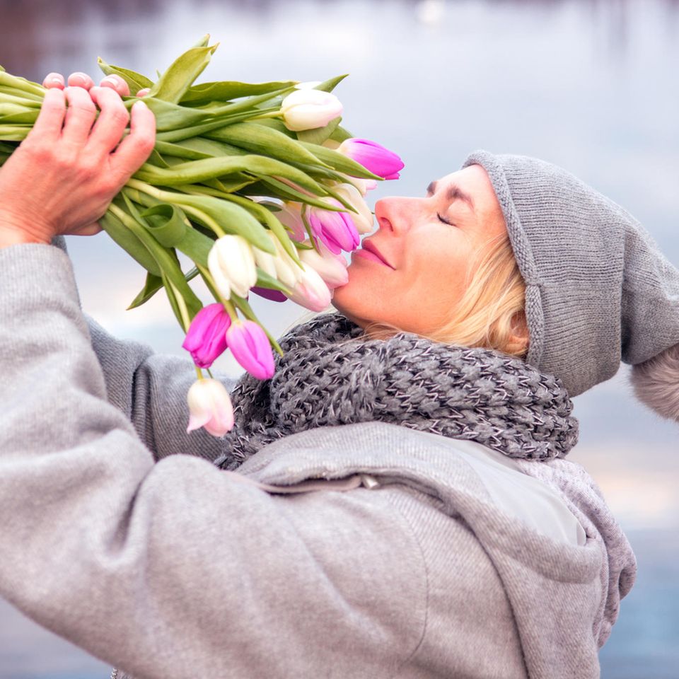 Oster-Horoskop ab 29.3.: Eine fröhliche Frau riecht an einem Strauß Tulpen