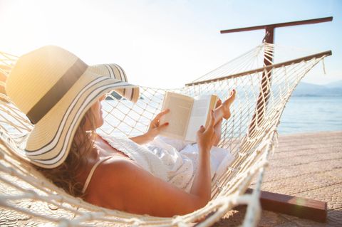 Frau liest in einer Hängematte am Meer: 5 Bücher, die Lust aufs Reisen machen