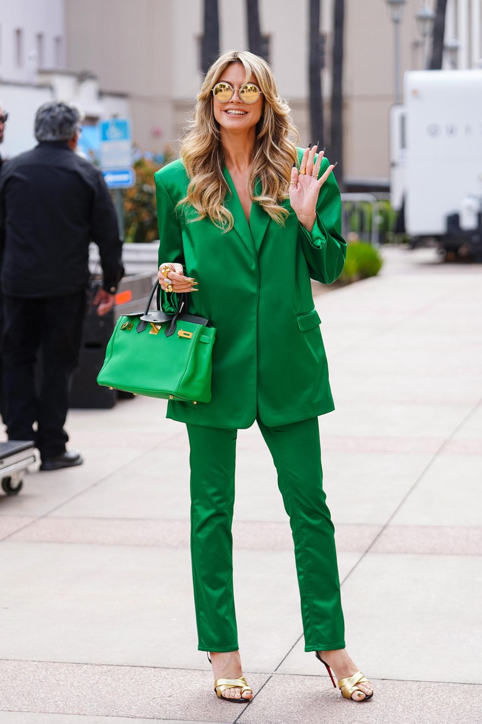 Heidi Klum setzt auf einen grünen Hosenanzug, den sie mit einer grünen Birkin Bag und goldenen Heels komplettiert. 