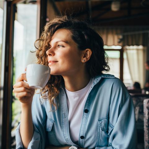 Frau trinkt entspannt Kaffee und schaut aus dem Fenster: 4 simple Wege, weniger hart zu dir zu sein