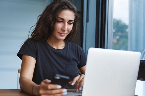Altersvorsorge und ETF: Junge Frau schaut in einen Laptop und hat ein Handy in der Hand