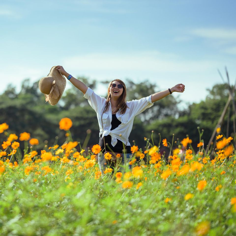 Horoskop ab 21.4.: Eine fröhliche Frau in einem Blumenfeld
