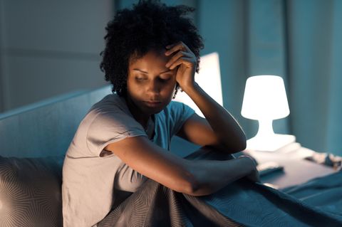 Unzufrieden mit dem Leben: junge Frau sitzt unglücklich auf dem Bett