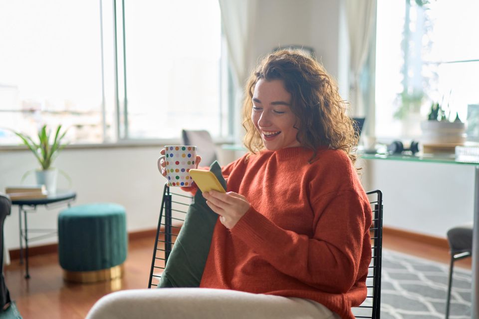 Lachende Frau mit Becher und Smartphone: Diese 5 Gedanken haben erfolgreiche Menschen täglich