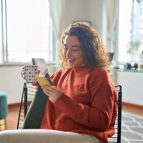 Lachende Frau mit Becher und Smartphone: Diese 5 Gedanken haben erfolgreiche Menschen täglich