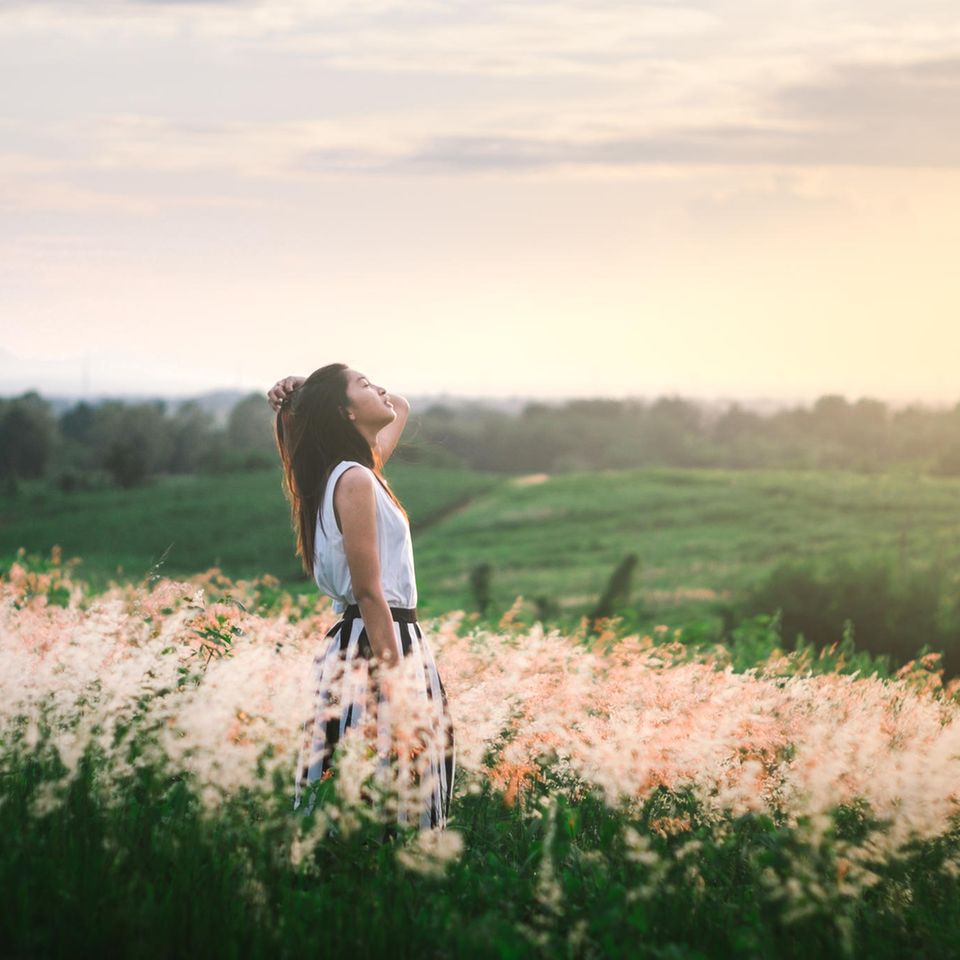 Wochen-Horoskop ab 29.4.: Eine Frau steht auf einem Feld und genießt die Sonne