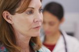 Die größten Irrtümer über die Wechseljahre: Eine kritisch und besorgt schauende Frau, im Hintergrund eine Ärztin