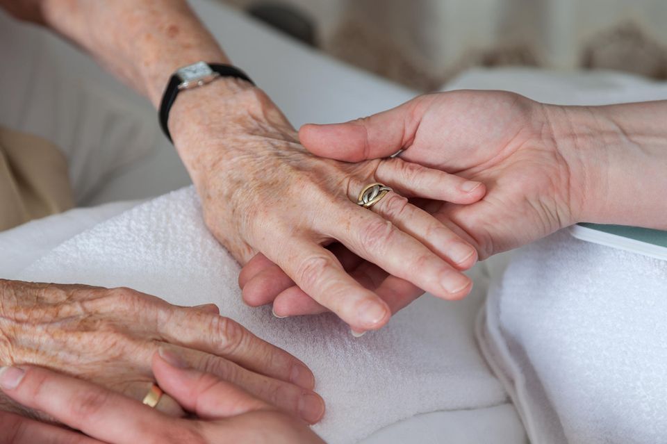 Pflege zu Hause: Zwei Hände halten die Hände einer älteren Dame