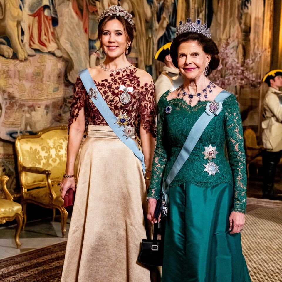 Beim Staatsbankett in Schweden, zu Ehren des dänischen Königspaares, strahlen Königin Mary und Königin Silvia in ihren prächtigen Roben. Als Ehrengästin trägt Königin Mary einen goldenen Seidenrock, den sie mit einem Oberteil aus rubinroten Verzierungen kombiniert. Passend zum Rubinrot verziert die Ruby Parure Tiara das Haupt der dänischen Königin und verpasst ihr ein majestätisches Auftreten. Königin Silvia hingegen glänzt in einem smaragdgrünen Spitzenkleid von "Georg et Arend", das sie elegant mit blauen Saphiren in ihrer Leuchtenberg-Saphir-Tiara und ihrem Halsschmuck kombiniert. Beide Königinnen verkörpern nicht nur Eleganz, sondern auch die wertvollen Verbindungen zwischen ihren Nationen, was die Pracht dieses besonderen Anlasses unterstreicht.